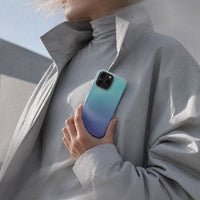 Kvinne i grå kåpe som holder en iPhone 16 Pro Max med Himmeldis mobildeksel i blågrønn og lilla gradient.