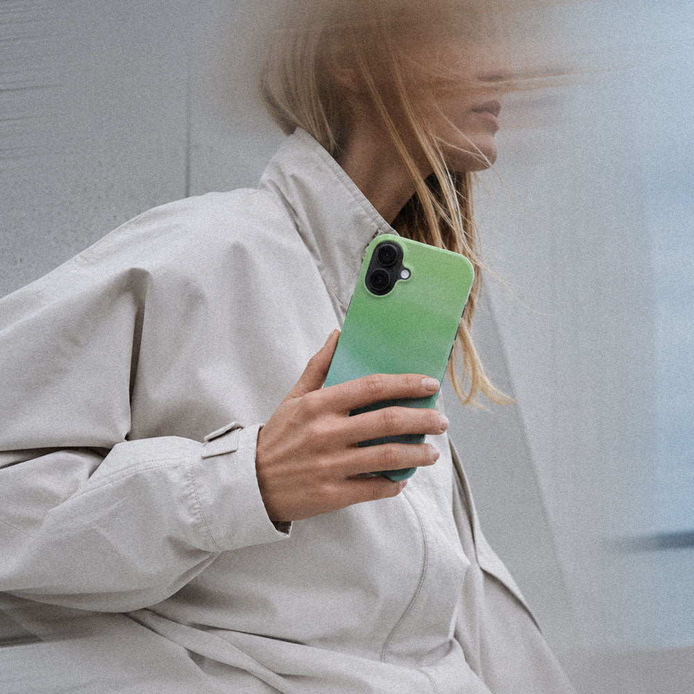 Kvinne i lys jakke som holder en iPhone med Myntdis mobildeksel i mintgrønn gradient.